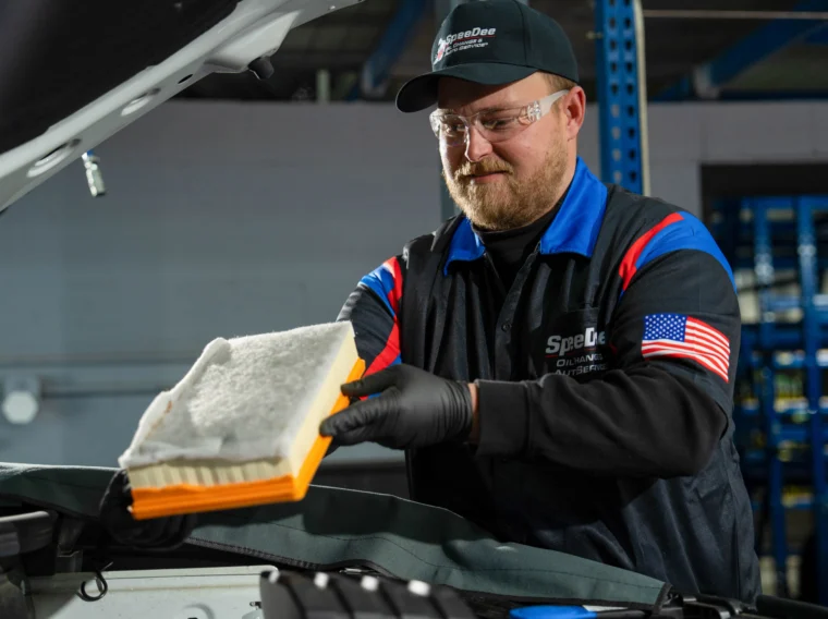 A mechanic wearing safety glasses and gloves removes a dirty air filter from a car engine, performing professional Filter Services in an auto repair shop.