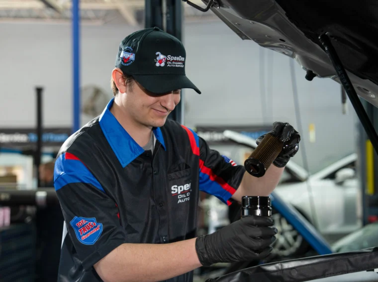 A mechanic wearing gloves and a uniform pours oil into a car engine while working in an auto repair shop, where filter services are also expertly handled.