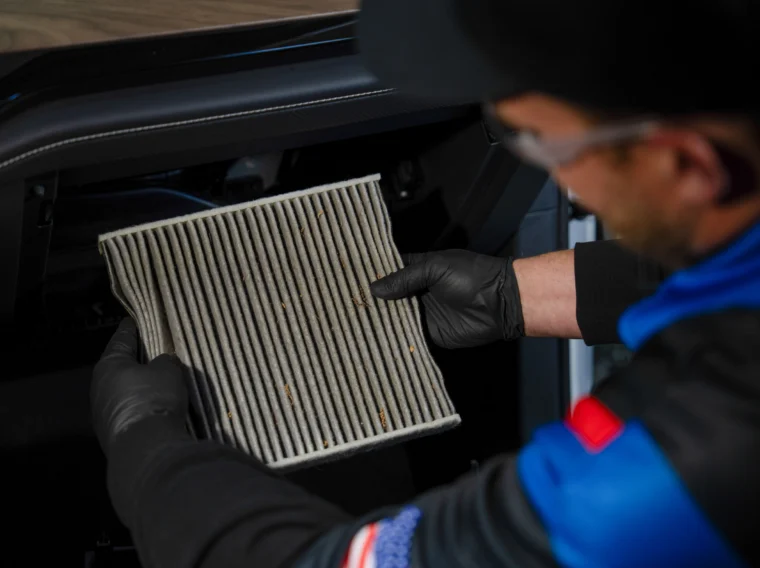 A person wearing gloves removes a dirty cabin air filter from a car’s glove compartment area, showcasing professional Filter Services.
