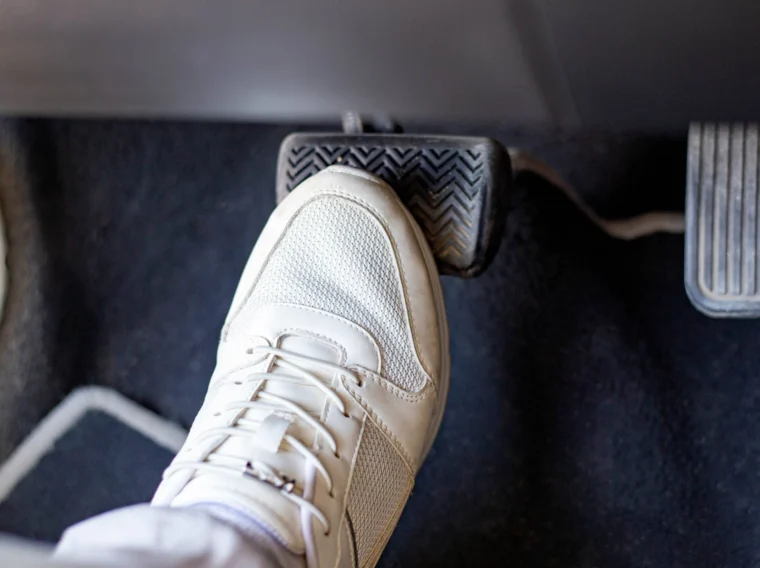 A person wearing a white sneaker presses down on a car's brake pedal inside a vehicle, perhaps after a recent cylinder replacement.