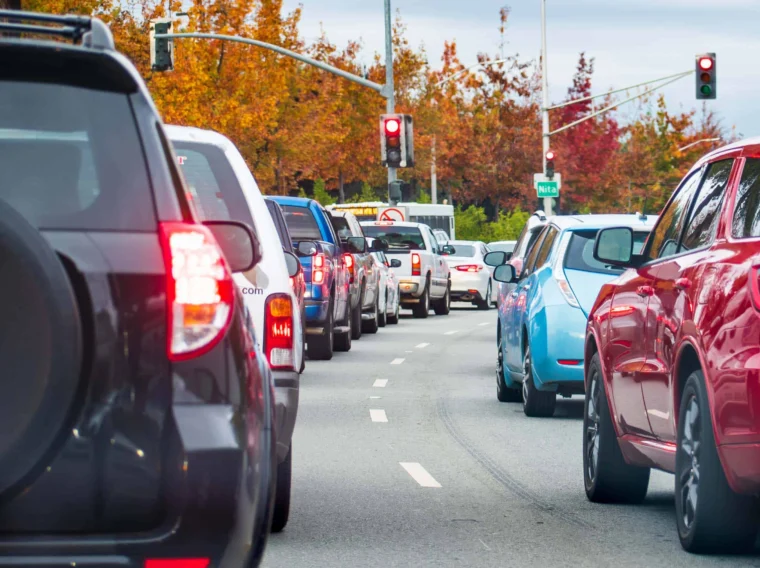 Cars lined up at a red traffic light on a multi-lane road, with autumn trees and traffic signals in the background—perfect timing to think about essential car care like clutch replacement.