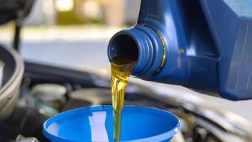 Motor oil being poured from a blue container into a blue funnel placed in a car engine compartment.