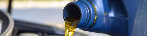 Motor oil being poured from a blue container into a blue funnel placed in a car engine compartment.