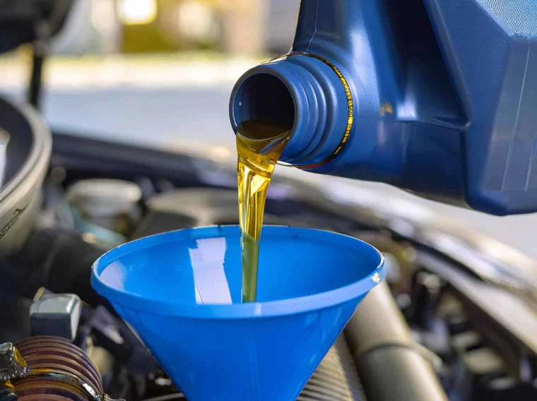 Motor oil being poured from a blue container into a blue funnel placed in a car engine compartment.