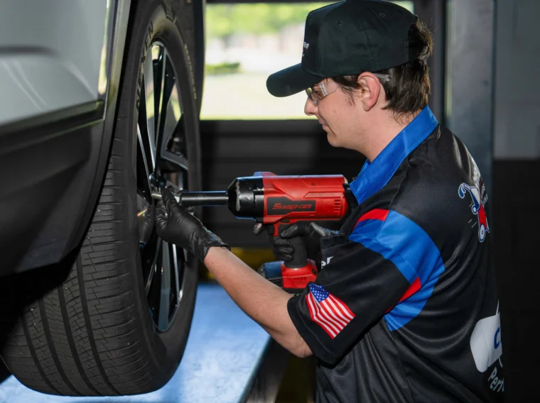 A mechanic provides tire services by using a power tool to tighten lug nuts on a car wheel in an auto repair shop.