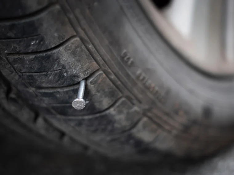 Close-up of a car tire with a large silver nail embedded in the tread, highlighting the need for professional Tire Services.