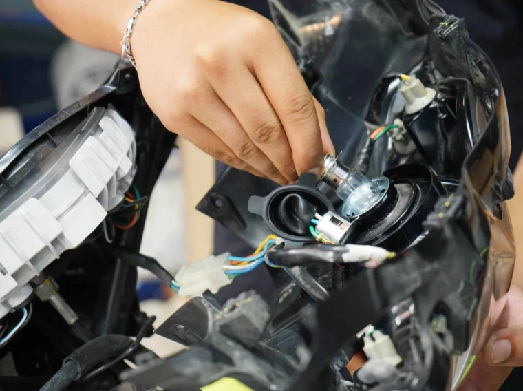 A person’s hand installs or removes a light bulb inside a car headlight assembly with visible wiring, demonstrating expert Lighting Services.