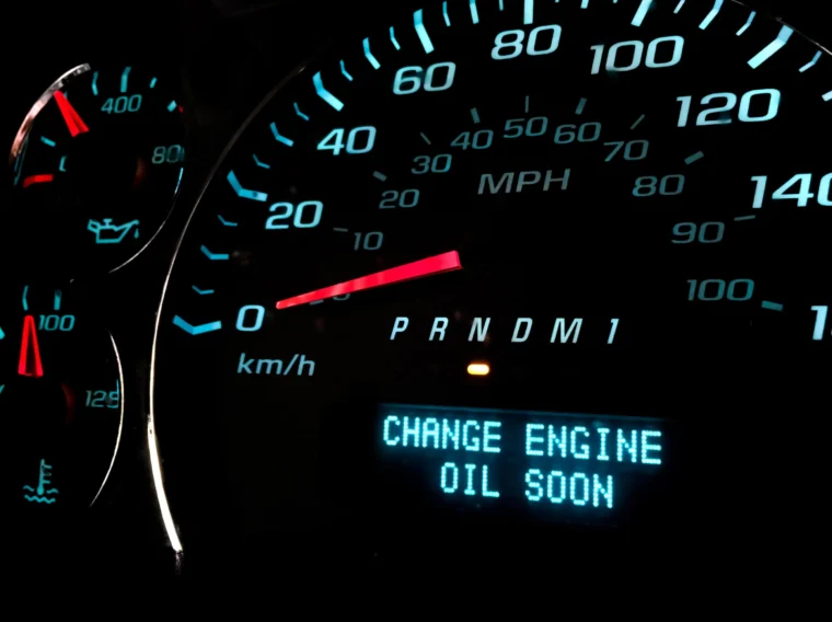 Close-up of a car dashboard showing speedometer, gear indicator, and a warning message that reads "CHANGE ENGINE OIL SOON.