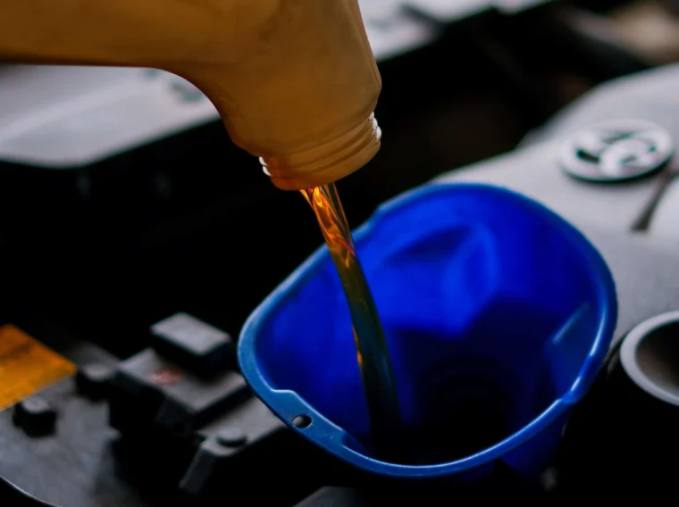 Motor oil is being poured from a plastic container into a blue funnel placed in a car engine compartment during Fluid Exchange Services.