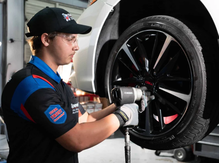 A mechanic performs tire services, using a power tool to tighten lug nuts on a car tire in an auto repair shop.