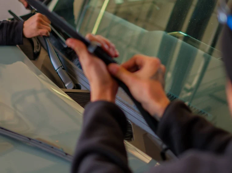 Two people are installing or replacing a windshield wiper blade on the front windshield of a car, an important step often checked during State Inspection Services.