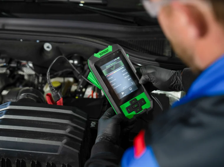 A mechanic uses a handheld diagnostic scanner to check a vehicle’s engine system under the hood as part of thorough tune up services.