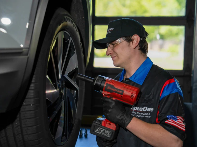 An auto technician uses a red power tool to tighten a lug nut on a car wheel in a service garage, ensuring precise results as part of their expert alignment services.