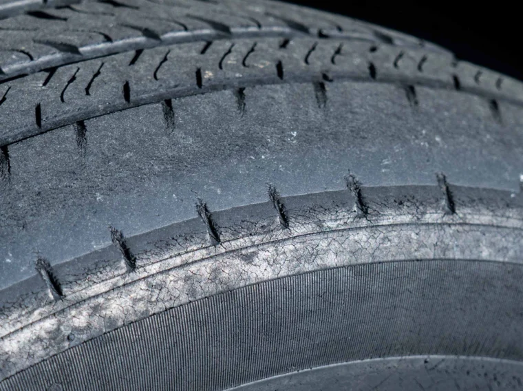 Close-up of a worn car tire showing significant tread wear and visible cracks, indicating the need for replacement and possible alignment services.