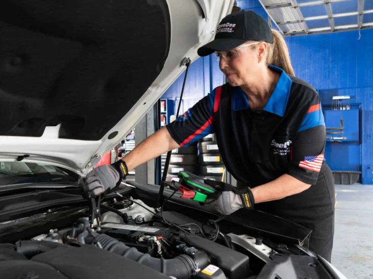 A mechanic in uniform inspects a car engine with diagnostic equipment inside a garage, ensuring compliance with the manufacturer’s maintenance standards.
