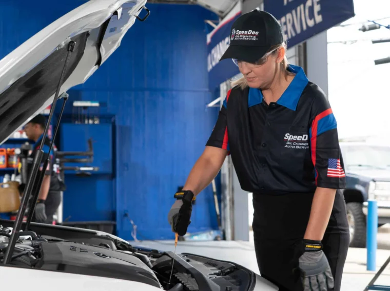 An auto technician checks the oil level of a car engine inside a service garage as part of the manufacturer’s maintenance schedule.