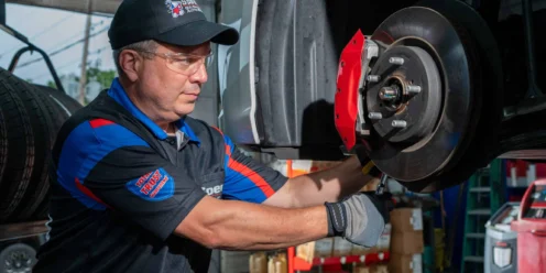An auto mechanic in uniform and safety glasses works on the brake assembly of a car in a garage.