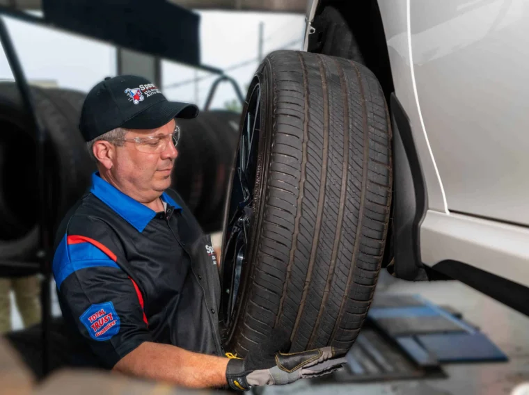 A mechanic wearing safety glasses and gloves is removing a car tire in an auto repair shop.