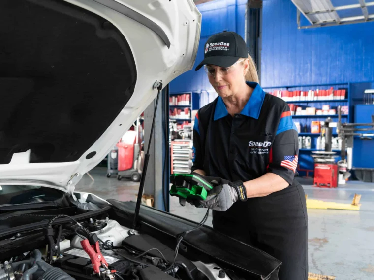 A mechanic in uniform uses a diagnostic tool to check a car engine in an auto repair shop, ensuring quality Tune Up Services for optimal vehicle performance.