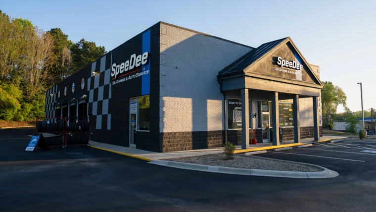 A SpeeDee Oil Change & Auto Service building with a checkered design, large windows, and a sign above the entrance, set in a parking lot on a sunny day.