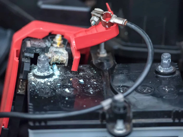 A car battery with corrosion on the terminal, partially covered by a red plastic cap, with attached cables visible—an example of when professional battery services may be needed.