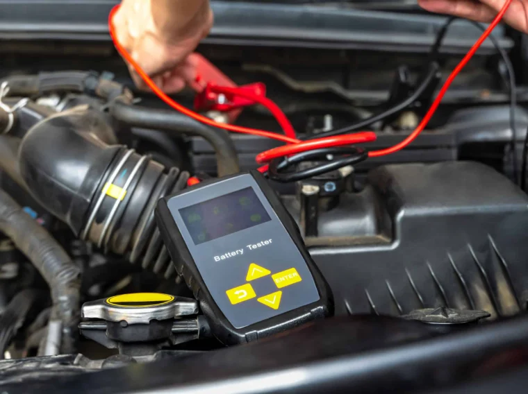 A person uses a digital battery tester with red and black cables to check a car battery under the hood, demonstrating reliable Battery Services for vehicle maintenance.