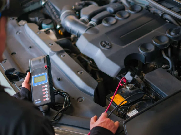 A person uses an automotive diagnostic tool to test a car battery under the hood of a vehicle.